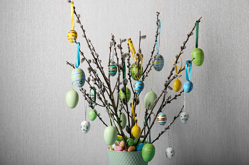 Beautiful willow branches with painted eggs on light grey background, closeup. Easter decor
