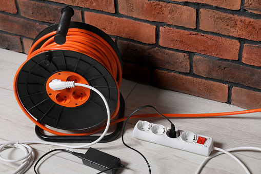 Extension cord reel on white floor near brick wall. Electrician's equipment