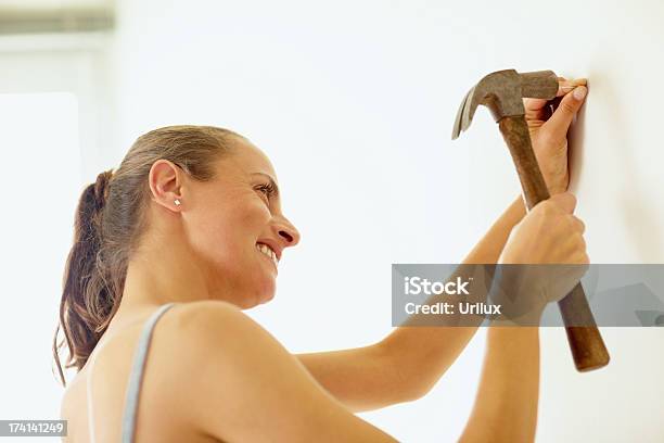 Woman Hitting A Nail Into A Wall Using A Hammer Stock Photo - Download  Image Now - Adult, Beautiful People, Beautiful Woman - iStock