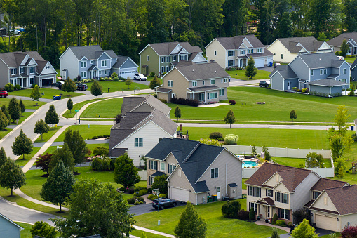 Low-density two story private homes in rural residential suburbs outside of Rochester, New York. Upscale suburban houses with large lot size and green grassy lawns in summer season.