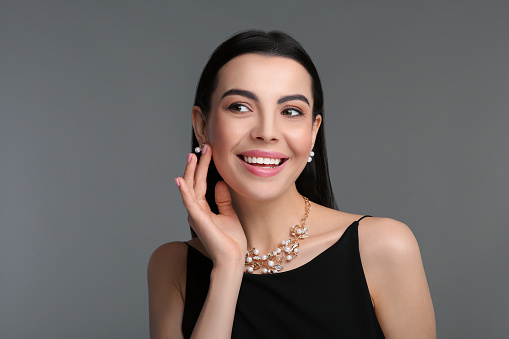 Beautiful young woman with elegant jewelry on dark grey background