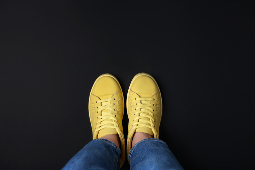 Woman in stylish sneakers on black background, top view