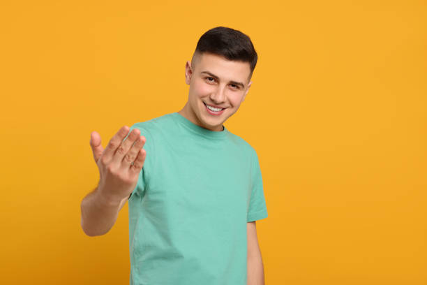 istock Handsome man inviting to come in against orange background 1741437744