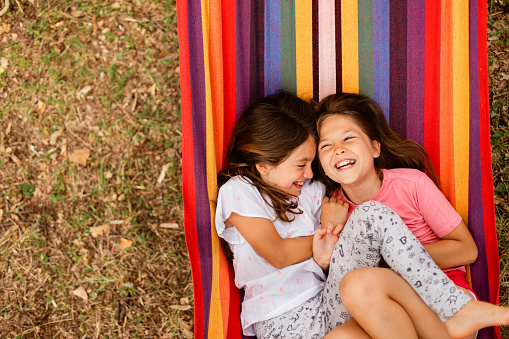 Above shot of two girls smiling and having fun while lying in the hammock in the yard