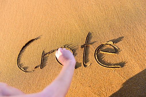 Young woman is writing word Crete on the sand in sunset.