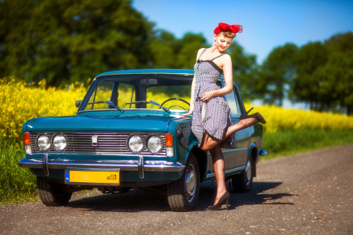 Beautiful young woman posing with old Polish (Italian) car in rural scenery.