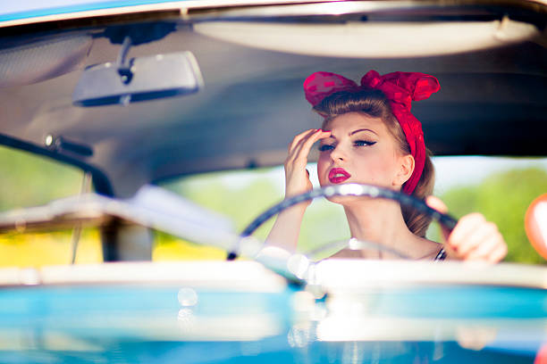 Pin-up girl in car Retro-styled image of a beautiful young woman sitting in car, correcting her make-up. pin up girls and cars stock pictures, royalty-free photos & images