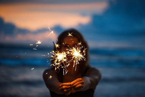 Happy young woman holding sparkler celebrating new years eve on the beach