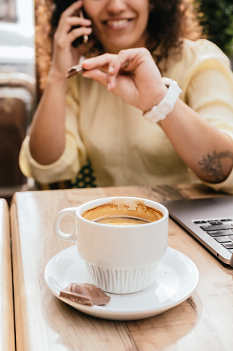 close-up of cup of coffee and woman in background talking on cell phone