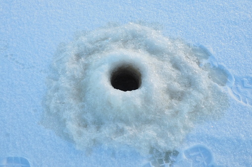 Winter fishing in January. A round hole in the ice and snow, made with an ice pick. Hobby, sports or amateur fishing. Danger of falling into cold water. Brittle ice.