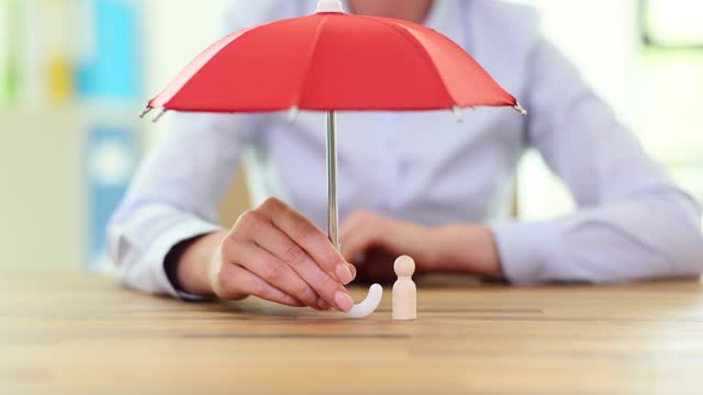 Woman places red umbrella over single wooden human figure