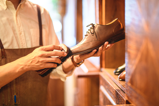 Hands of a man polishing high quality leather shoes. He is working in a luxury fashion store that sells shoes and clothes for mature men with elegant and classy style. The shoes are handmade by artisans and shoemakers.