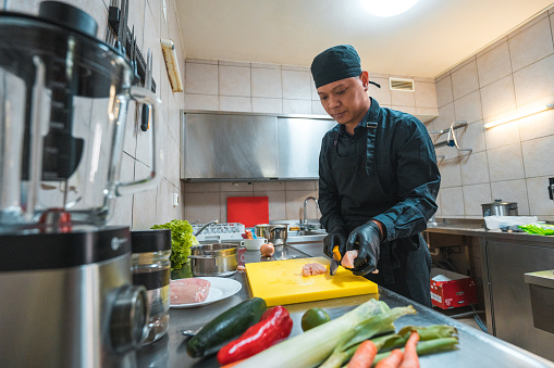 Man working as a chef at an asian kitchen. He is easily cutting vegetables for a recipe.