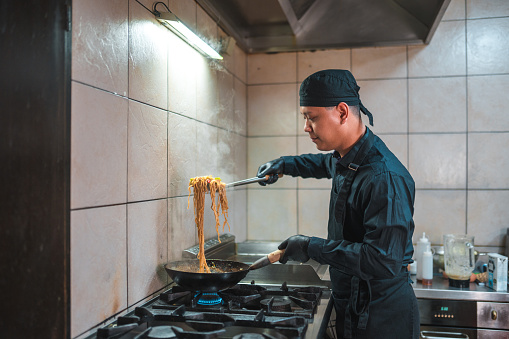Asian chef cooking a symphony of flavors and textures inside the asian kitchen. He is wearing black gloves and uniform.