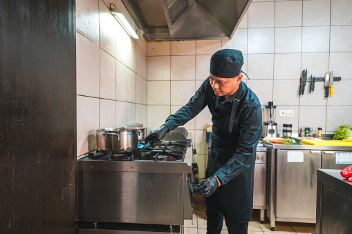 Three quarter length shot of an indonesian chef. He is using a gas stove in the asian restaurant.