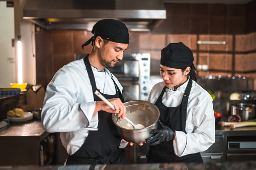 Waist up shot of mature Asian chefs using their years of experience to create delicious dishes. They are wearing a white uniform and black apron.