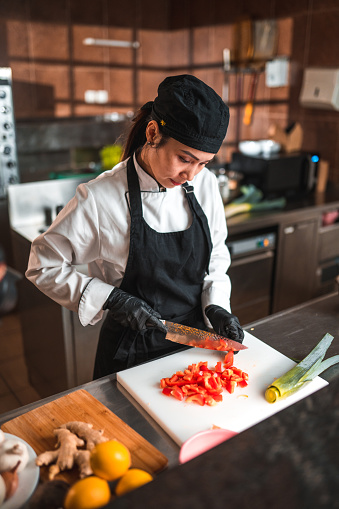 Waist up portrait of female chef, who is an expert in her craft, as she dices red peppers for her signature dish.