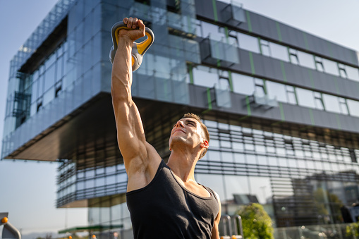 One man young caucasian male muscular athlete stand outdoor in day training with russian bell girya kettlebell weight exercise strength and conditioning endurance real person copy space