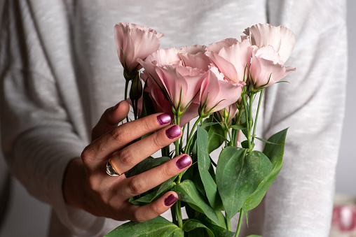 Female hands holding a bouquet of light pink flowers with fresh green leaves