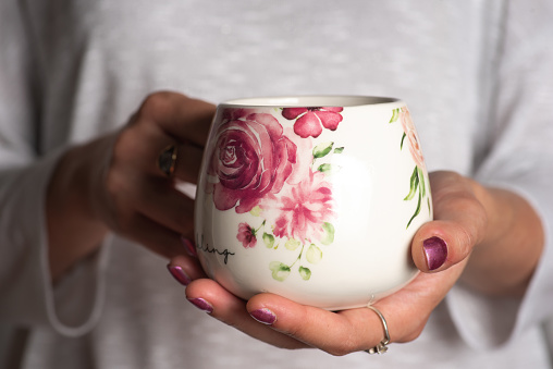 Female hands holding a white cup with pink flowers, for tea or coffee. Small copy space for advertising text message or promotional content