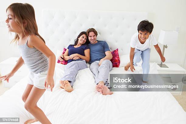 Los Niños De Padres Salto En Cama Usando Pijama Foto de stock y más banco de imágenes de Cama - Cama, Rebotar, 20 a 29 años