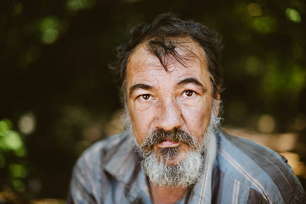 Close up picture of a man with a beard real homeless man on the foliage background, selective focus on eye homelessness photos stock pictures, royalty-free photos & images