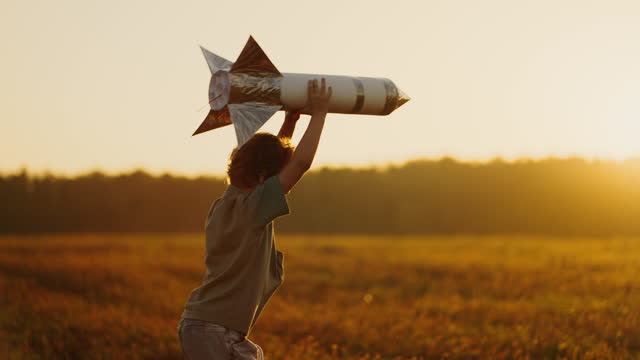 Fantasy And Dream Of Space Travel, Child Boy Playing With Handmade Rocket In Meadow