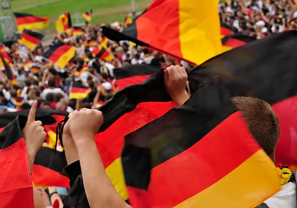 Photo of Soccer fans in a stadium waving German flags.