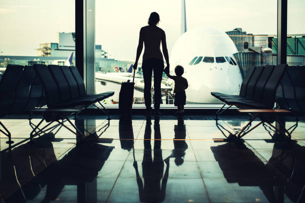 Mother and Son at Airport A picture of a woman and her little boy standing holding hands with their suitcase in a waiting area lobby at the Frankfurt airport, a large plane visible through the big bay windows.  High contrast leaves just their silhouettes visible.  Meant to depict travel with a child or infant.  Horizontal image. frankfurt international airport stock pictures, royalty-free photos & images
