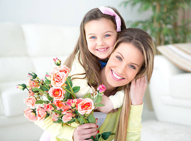 Cute daughter giving her mother flowers for Mother's Day. Looking at camera.