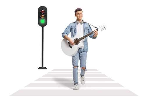 Young male playing an acoustic guitar and crossing a street at a pedestrian crosswalk isolated on white background