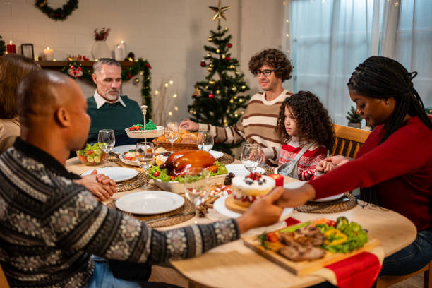 istock Multi-ethnic big family saying a prayer before having Christmas dinner. Attractive diverse group of people having dinner eating food to celebrate holiday Thanksgiving X-mas eve on dining table at home 1741866639