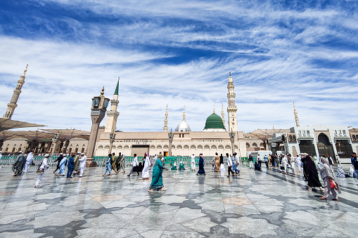 Medina, Saudi Arabia - March 10, 2023: Muslim pilgrims walk in the courtyard of Masjid al-Nabawi (Prophet's Mosque). As the final resting place of the Prophet Muhammad, it is considered the second holiest site in Islam by Muslims (the first being the Masjid al-Haram in Mecca).
