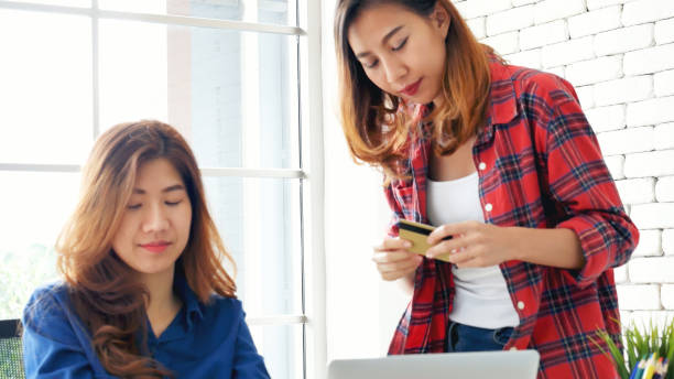 dwoje przyjaciół robiących zakupy za pomocą karty kredytowej online na stronie laptopa e-commerce z uśmiechniętą twarzą, szczęście. szczęśliwe azjatyckie kobiety korzystające z zakupów na laptopie kupno online, płatność nowanormalna koncep - e commerce couple working at home internet zdjęcia i obrazy z banku zdjęć