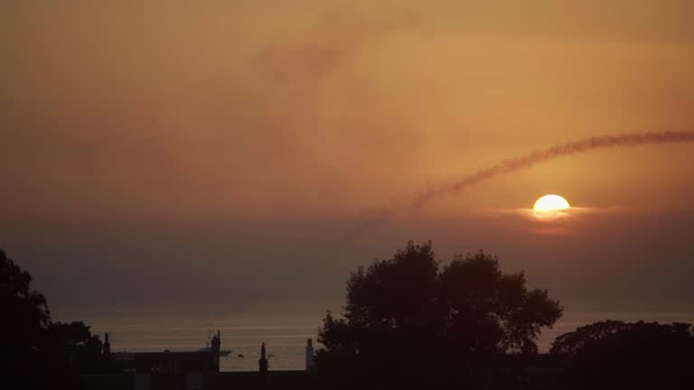 Sunsets in the distance as a Gyrocopter flies over the silhouettes of trees below