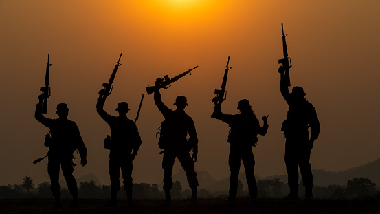 silhouette group of special forces sodiers standing and holding gun over the sunset and colorful orange sky background, special warfare training operations teams,