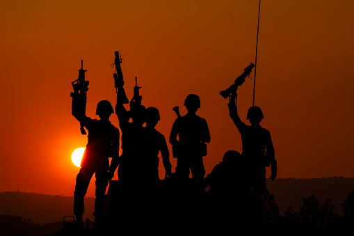 silhouette group of special forces sodiers standing and sit holding gun on cannon tank with over the sunset and colorful orange sky background, special warfare training operations teams,