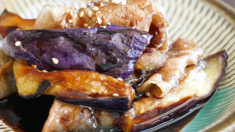 A video of pouring kabayaki sauce onto stir-fried eggplant and pork. Close-up. From left to right.