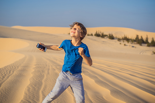 Cute funny boy in dance with a smartphone in his hands in the desert.