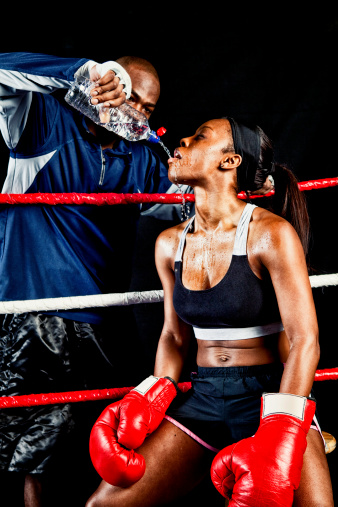 Female boxer getting water from her coach in the ring during a bout.