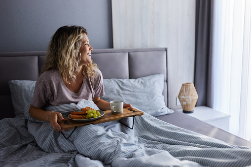 Happy woman day dreaming while relaxing during morning snack in a bed.