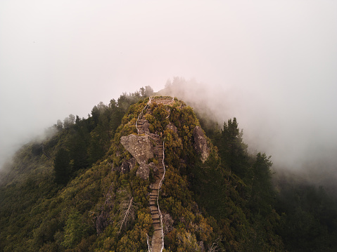 High angle view of young woman walking up the stairs on a mountain during foggy day. Copy space.