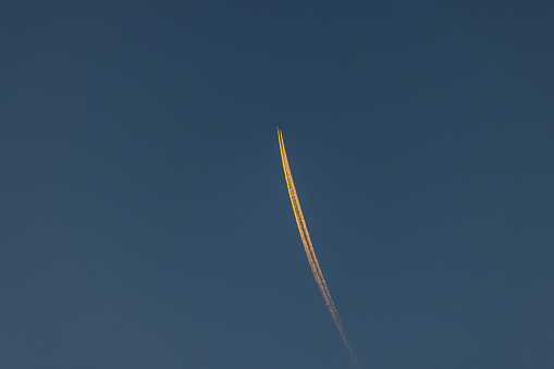 Plane is flying on blue sky at sunset.