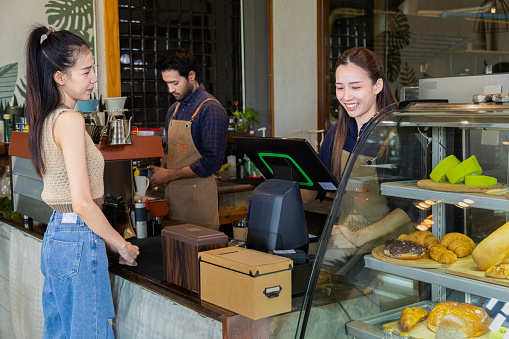 Small business startup young couple lifestyle concept, coffee owner husband and wife happy receive orders from counter in coffee shop, attractive customer female standing in front of bakery counter