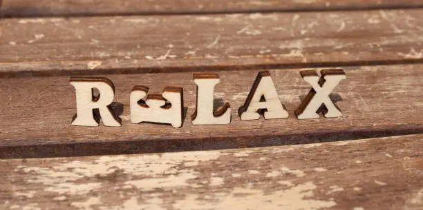 nature wooden letters in the sun on a sunny day. create the word: RELAX from wooden letter alphabet. background is made from naturally wood.