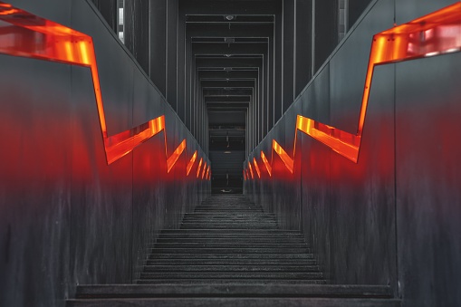 A dimly lit, red-glowing hallway with a staircase ascending up the side