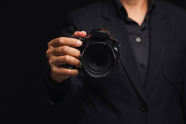 istock Photographer in a suit holding the digital camera while standing on a black background 1742150680