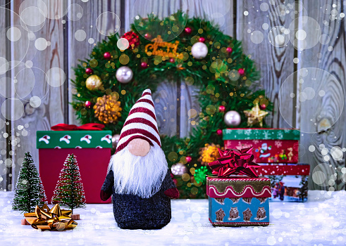 Christmas gnome (elf) with gift boxes, golden and red ribbon, Christmas wreath and Christmas trees. Merry Christmas concept with bokeh