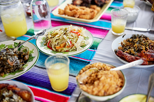 Close view of drinking glasses filled with lemonade surrounded by hearty Jamaican meat, seafood, and vegetable dishes.