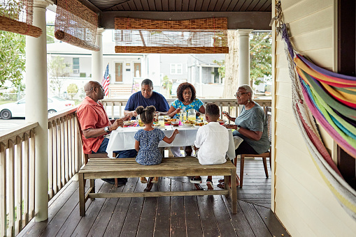 Full length view of children, parents, and grandparents seated around dining table on porch of home in Rockaway Beach, Queens.